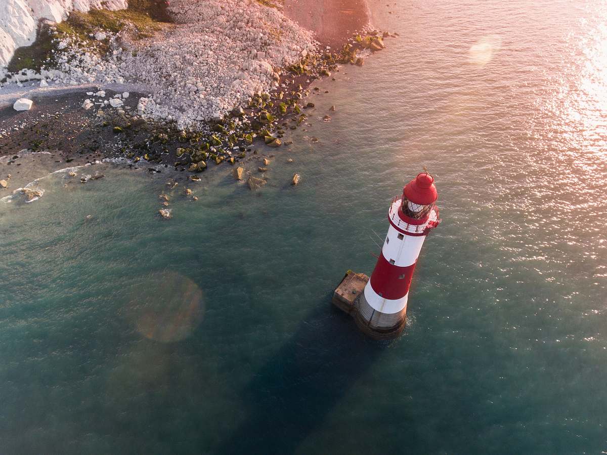 aerial view white and red lighthouse in body of water near shore lighthouse